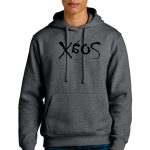 A person with short blond hair is wearing a dark gray hoodie featuring a stylized design on the chest. They are standing and looking forward, with their hand in the pocket of the hoodie.