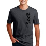 A person wearing a gray T-shirt with the word "Xaos" printed vertically in black on the side. They are smiling and have their hands in the pockets of their dark jeans against a plain white background.